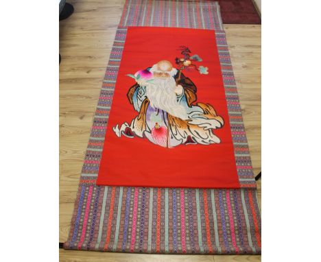 A LARGE CHINESE EMBROIDERED SCROLL depicting an immortal, laid on to decorative background, 10 ft x 4 ft, red area 195.5 101.
