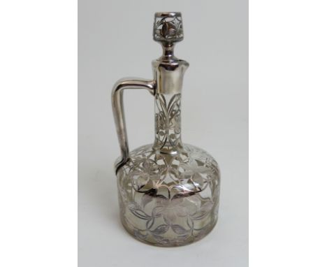 A CLEAR GLASS DECANTER bottle shaped, the body overlaid in unmarked silver flowerheads and tendrils with angled handle, 24cm 