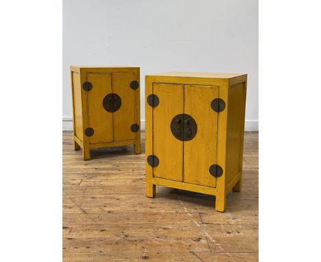 A pair of Chinese yellow lacquered bedside cabinets, each with two panelled doors enclosing  shelf, raised on stile supports,