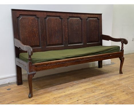 An 18th century vernacular oak settle, the four panel back above scrolled open arms and squab cushion, raised on turned front
