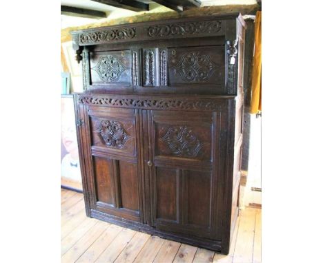 17th century carved oak court cupboard, the upper section with scroll carved pendant canopy and two relief carved doors with 