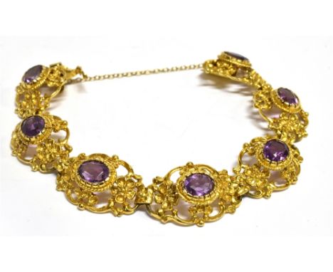 A 9 CARAT GOLD AMETHYST SET BRACELET  seven oval openwork links with scroll and flower head decoration, each set to centre wi