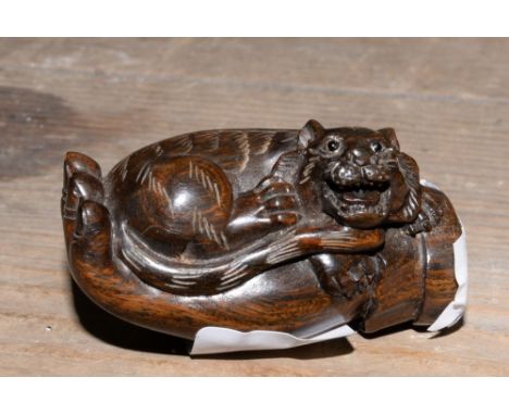 A Japanese dark wood carved Netsuke, depicting a hand holding a snarling Tiger type animal, signed to the base 