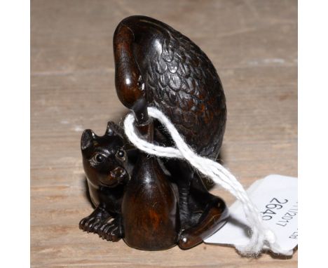 A Japanese dark wood carved Netsuke, depicting a Stork type bird drinking from a narrow necked bottle, the bird having a Dog 