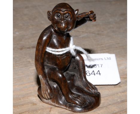 A Japanese dark wood carved Netsuke, depicting a Monkey holding a twig to his ear, signed to the base 