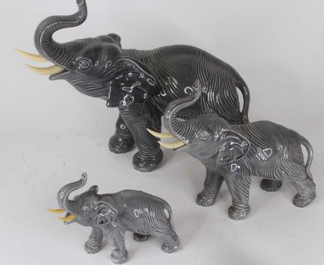 A graduated set of three pottery elephants, each modelled standing with trunk raised, the largest h.31cm