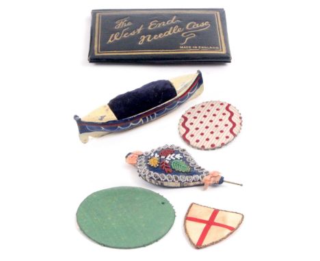 Five pin retainers and a needle book, comprising a cast metal and painted life boat pin cushion, 10cms, a bellow form pin cus