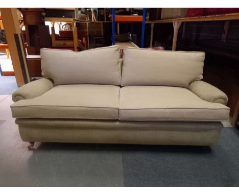 A contemporary Howard style sofa with scrolled arms raised on turned tapering mahogany supports terminating in brass casters.