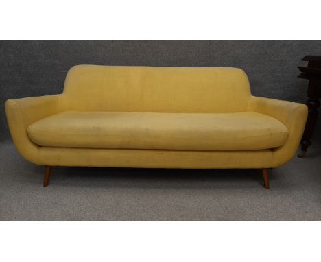 A 1960's vintage style three seater sofa of stylish curvilinear form, upholstered in yellow fabric on round splayed tapering 