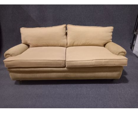 A contemporary Howard style sofa with scrolled arms raised on turned tapering mahogany supports terminating in brass casters.