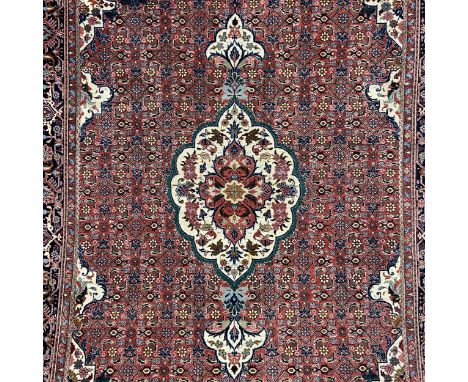 A silk Persian Bijar carpet having a central biscuit medallion with scrolling designs surrounded by repeating floral patterns