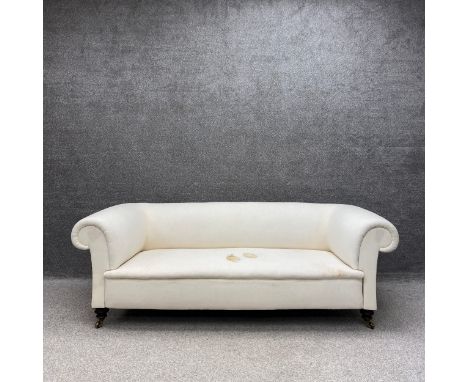 A Victorian three seater Chesterfield sofa upholstered in an off white calico with a scrolled back and arms raised on turned 