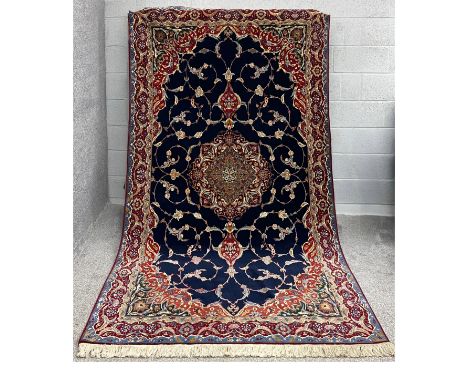 A large Persian silk Qum carpet with a central medallion surrounded by scrolling foliate decoration over a midnight ground su