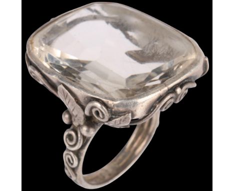 An Arts and Crafts silver rock crystal dress ring, set with oval flat-top rock crystal with floral shoulders, unmarked mount 