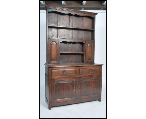 A Georgian style oak dresser of smaller proportions, the shaped cornice and arched frieze over two plate racks and cupboards,
