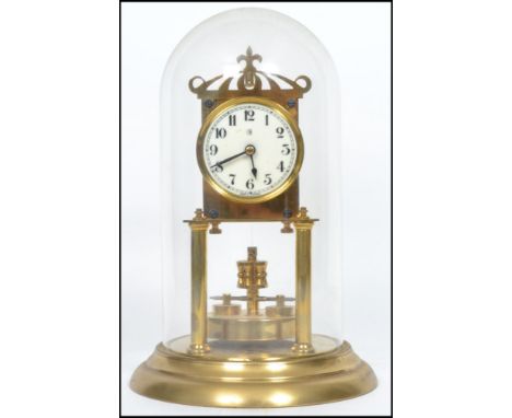 A 20th century glass domed brass anniversary clock raised on a stepped circular base with twin columns to front and fret pier