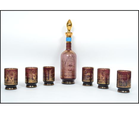 A 20th century studio art cranberry glass decanter and drinking glass set by Murano consisting of a decanter with gilt decora