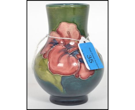 A Moorcroft baluster vase tube lined and decorated in the hibiscus pattern on a green and blue ground. The bulbous body raise