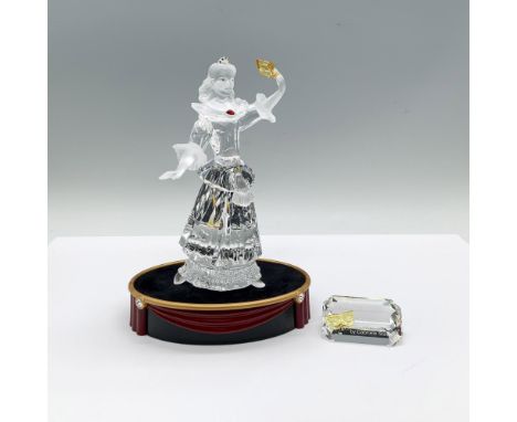 A clear and frosted figure of a theater character wearing a long dress costume. She is adorned with colorful crystals and is 