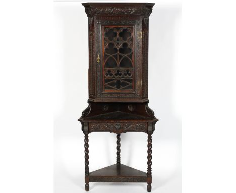 An Edwardian stained oak corner unit and a glazed corner display cabinet, the first engraved with flower heads, a mask and fr