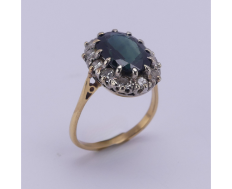 A sapphire and diamond cluster Ring, the oval facetted sapphire 11.3mm long, claw set above a surround of twelve circular dia