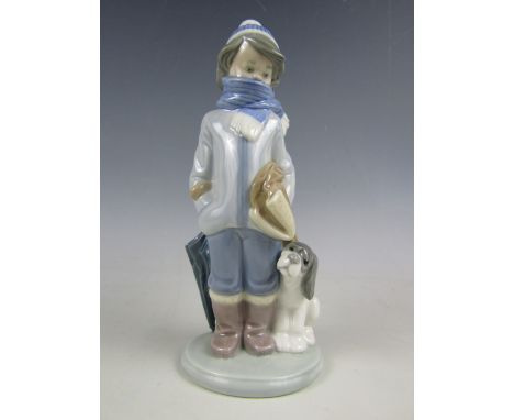 A Lladro figurine of a boy wearing a hat and scarf, with dog