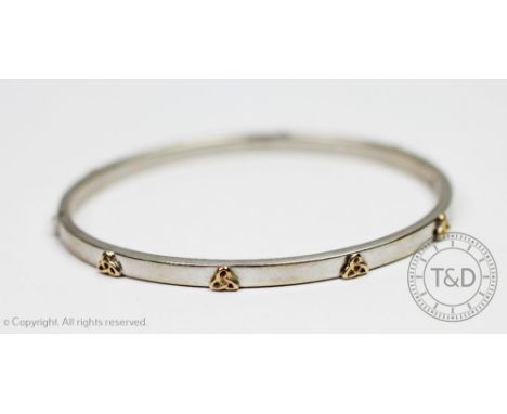 A white gold bangle, the hinged bangle set with eight yellow gold Celtic knots throughout, integral clasp stamped '375', gros