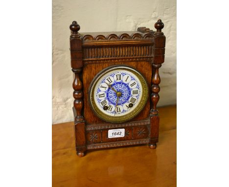 Continental oak cased mantel clock with turned decoration, having circular blue and white dial with Roman numerals and two tr
