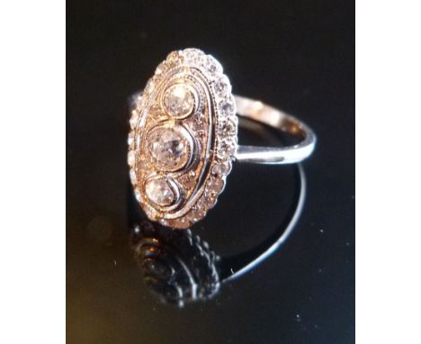 An 18ct. White Gold Art Deco Style Diamond Ring, with three central diamonds surounded by diamonds within an oval pierced set