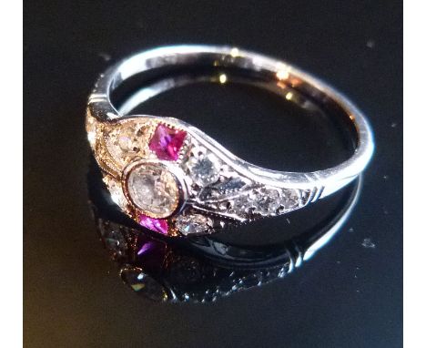 An 18ct. White Gold Ruby and Diamond Ring, in an Art Deco style with central diamond surrounded by diamonds and with two rubi