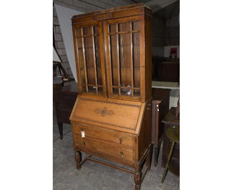 A 1920's oak bureau bookcase Having a caddy top above two glazed doors enclosing two adjustable shelves, the fall front centr