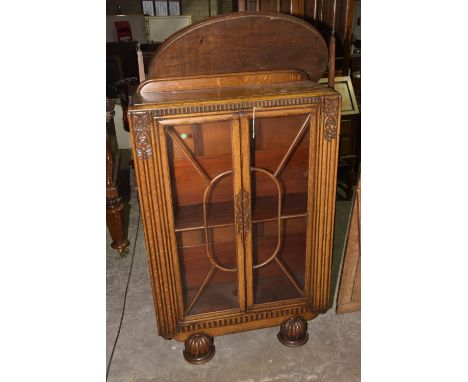 A Mid 20th Century oak display cabinetHaving two astragal glazed doors enclosing a single shelf flanked by carved decoration,
