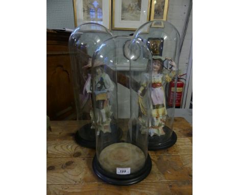 A pair of clear glass domes with turned stained wooden bases containing a pair of bisque figurines; a dancing girl and an org