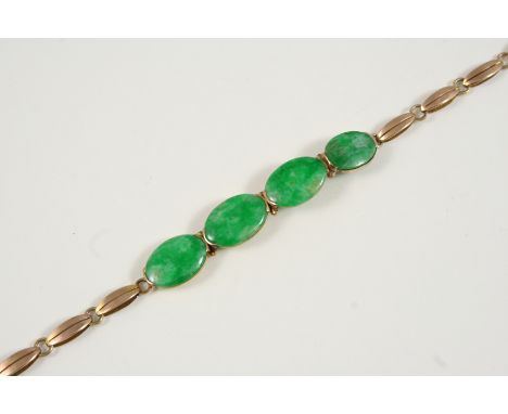 A JADE AND GOLD BRACELET formed with four oval sections of jade on a 9ct. gold fancy link bracelet, 17cm. long.