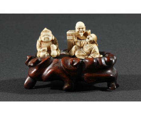 TWO JAPANESE IVORY NETSUKE, of demons appearing from a box and a seated figure, on a hard wood mount, height of demons 3.5cm