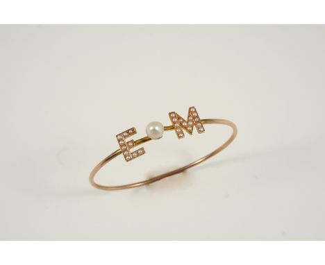 A GOLD AND PEARL SET BANGLE mounted with the initials E M set with half pearls and centred with a small pearl.