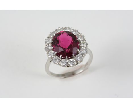 A TOURMALINE AND DIAMOND CLUSTER RING the pinkish red oval-shaped tourmaline is set within a surround of fourteen brilliant-c