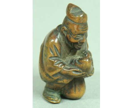 JAPANESE WOODEN NETSUKE OF A MAN CARRYING A BABY, resting on one knee, with carved swastika decoration, height 4cm