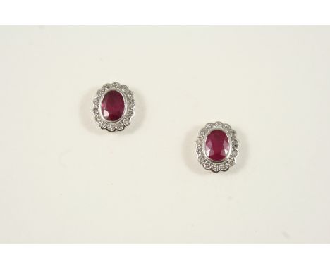 A PAIR OF RUBY AND DIAMOND CLUSTER STUD EARRINGS each set with an oval-shaped ruby within a surround of circular-cut diamonds