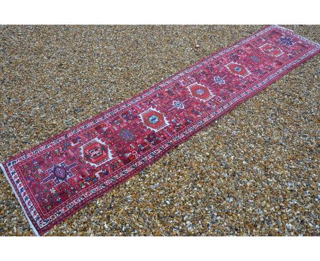 A Persian Shiraz runner with alternating medallions surrounded by flora and fauna motifs on red ground, guarded ivory border,