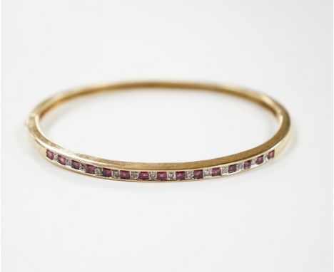 A yellow metal, ruby and diamond chip channel set hinged bangle, interior diameter 57mm, gross weight 10.8 grams.
