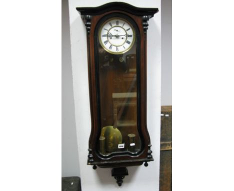 A XIX Century Walnut Vienna Wall Clock, with a white enamel dial, Roman numerals, glazed door, shaped base with finials.