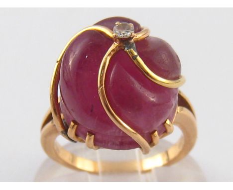 A yellow metal (tests 18 carat gold) carved ruby and diamond ring, ruby approx 14mm wide, ring size K ½, 7.7 gms.
