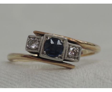 A lady's Edwardian style dress ring having a central sapphire flanked by two diamonds in square mounts to angular cross over 