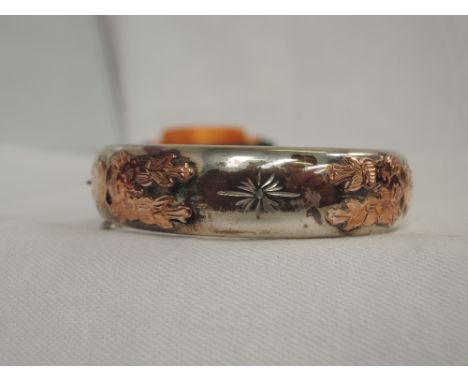 AN HM silver hinged bangle having yellow metal applique decoration