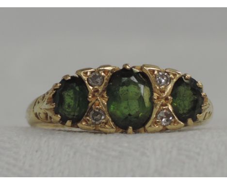 A lady's dress ring having three oval green stones, possibly tourmaline interspersed by diamond chips on a moulded gallery mo