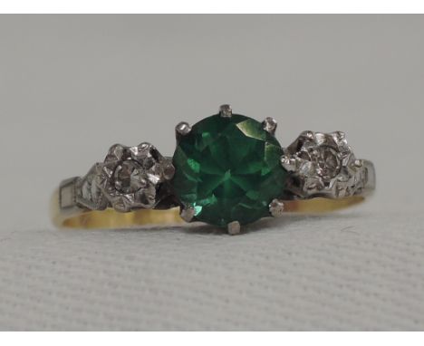 A lady's dress ring having a central green emerald style zircon flanked by two diamond chips to moulded shoulders on a yellow