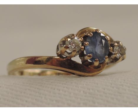 A lady's dress ring having a pale blue sapphire flanked by two diamonds in a claw set mount to crossover shoulders on a 9ct g