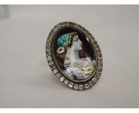 A lady's over sized dress ring having an enamelled panel depicting a maiden in profile on a white metal loop, no marks tested