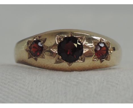 A yellow metal gypsy ring having three graduated inset garnets, marks worn but tested as 9ct rose gold, size W